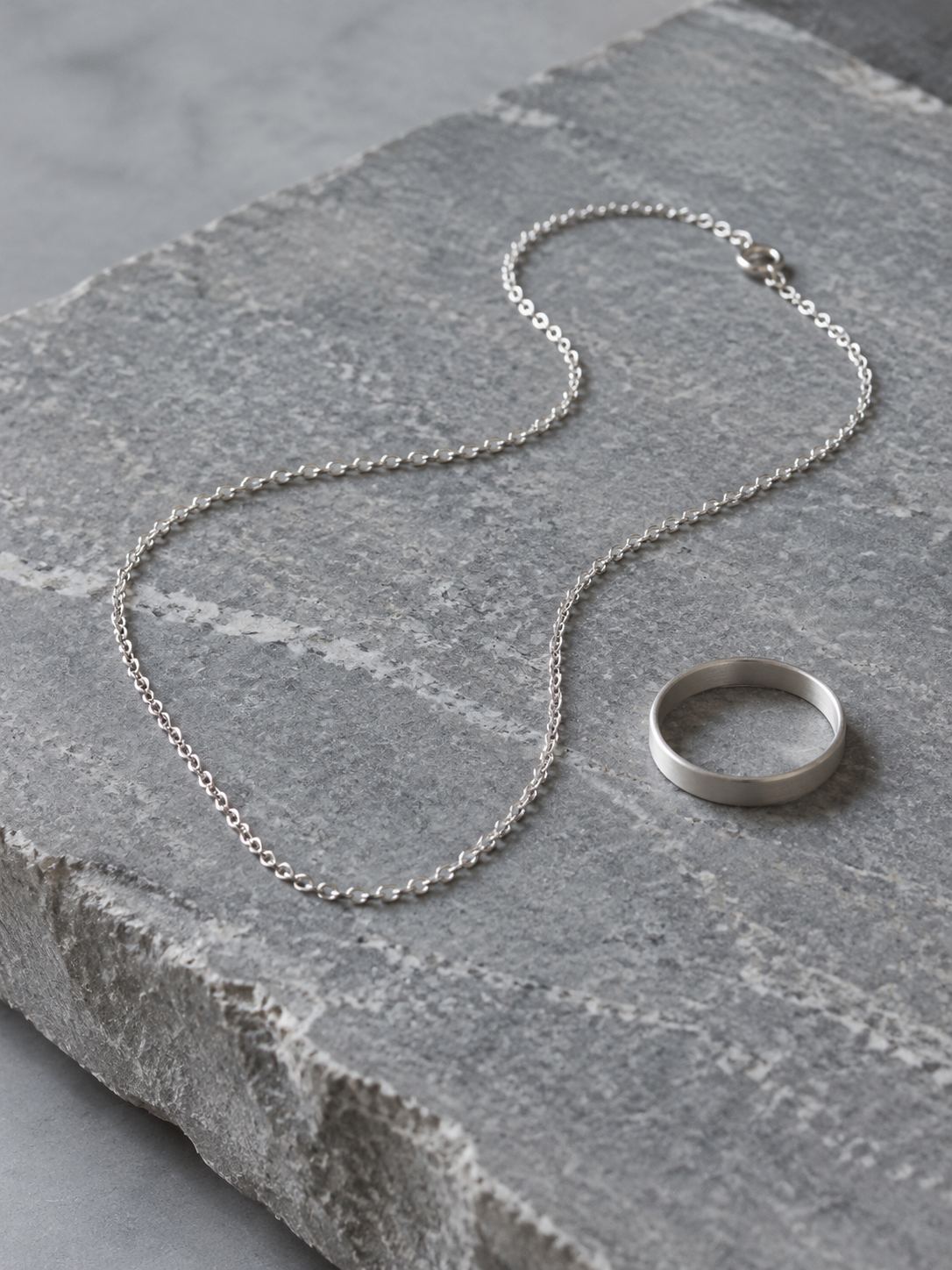 A silver chain and a plain metal ring on stone